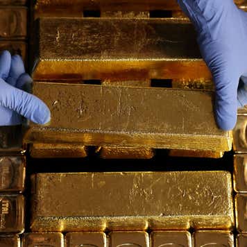 Pair of gloved hands lifting a gold bar.