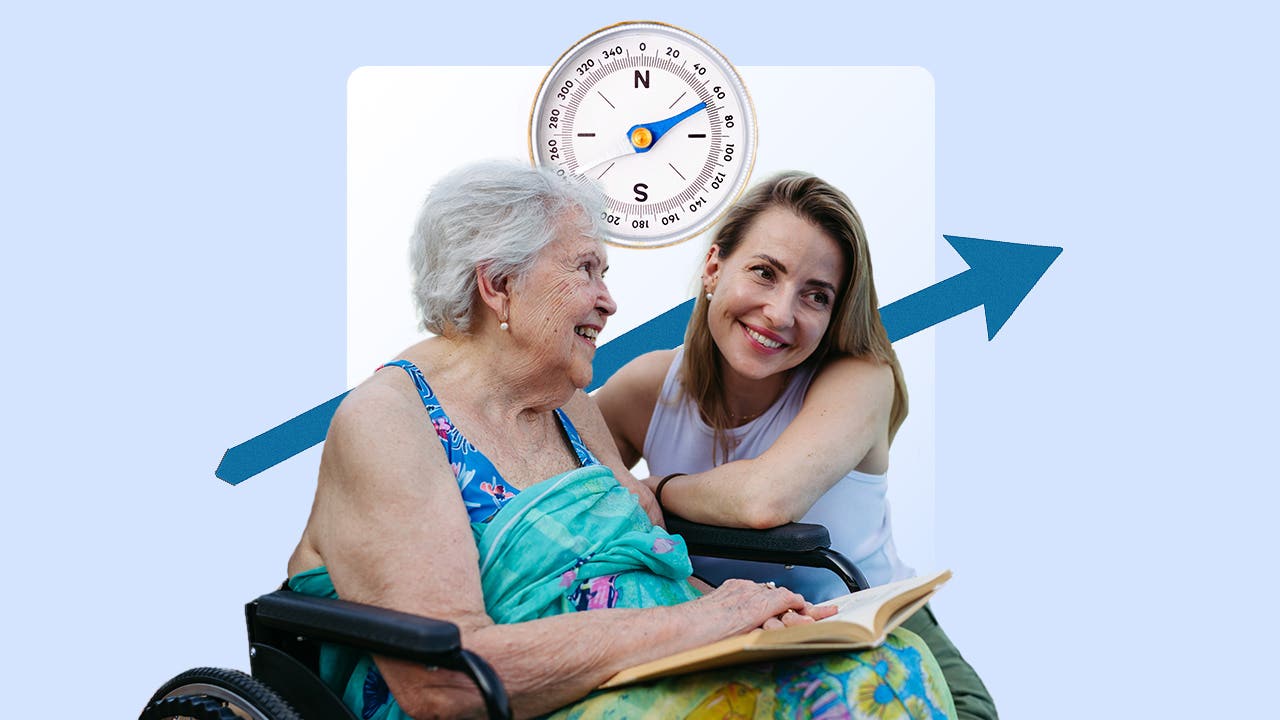 Image of an older woman sitting in a wheelchair reading a book with a younger women squatting down next to her. There is a large compass above and behind them .