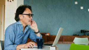 An older man looks at his investments on a laptop.