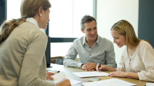 A couple signs papers across the desk from a loan agent.