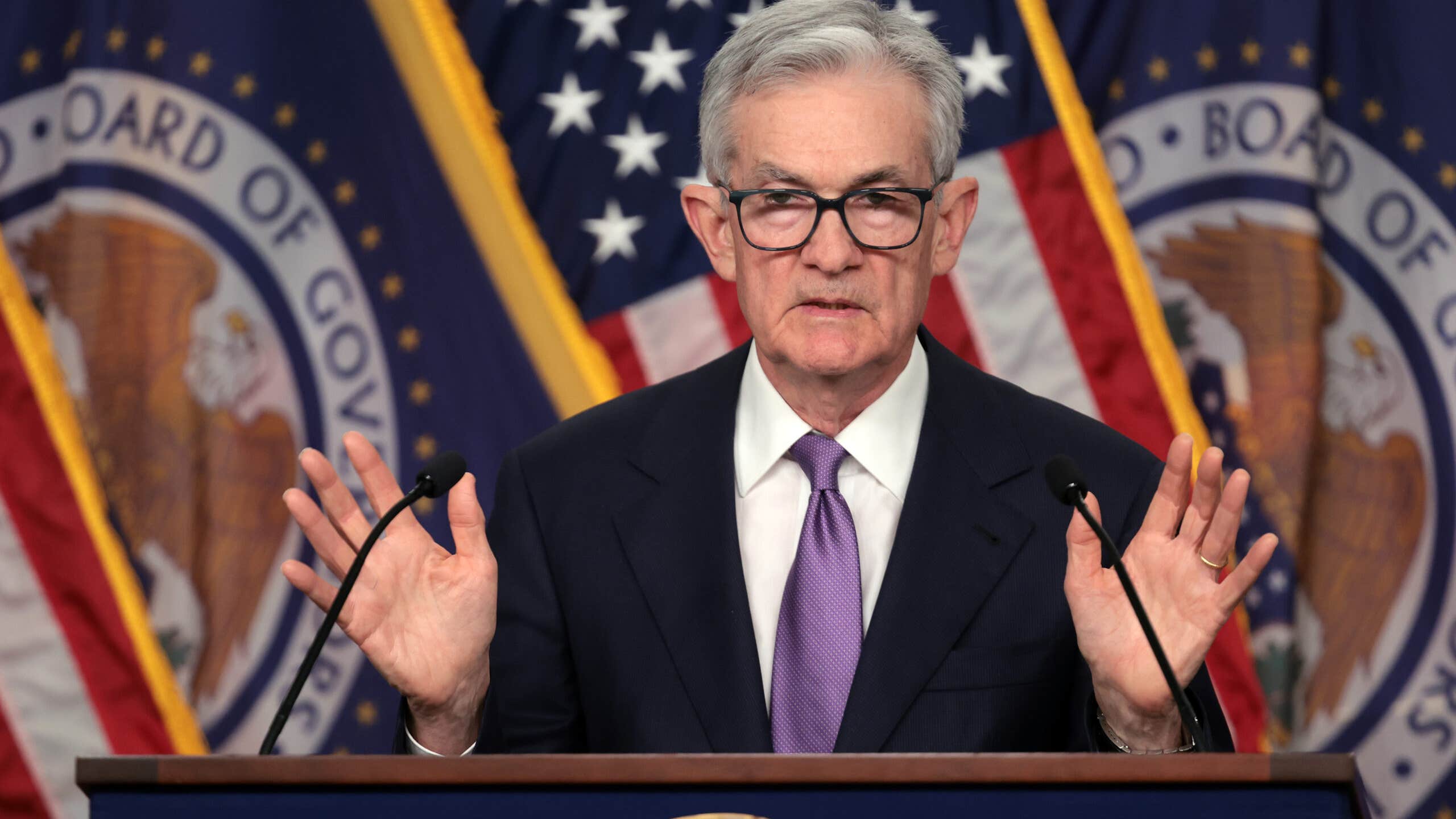 Photo of Fed Chair Jerome Powell at a podium, holding his hands up.