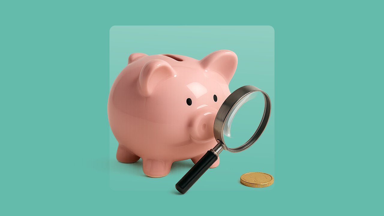 A piggy bank looks through a magnifying glass at a coin.