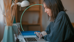 A woman sits at her desk and uses a laptop.