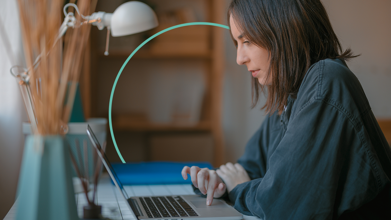 A woman sits at her desk and uses a laptop.