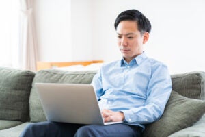 Man sitting on a couch looks at a laptop.
