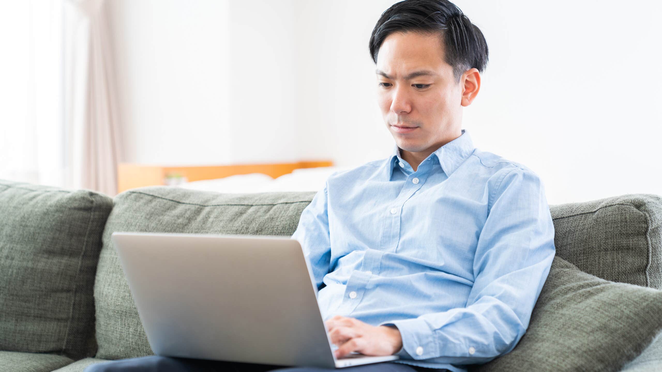 Man sitting on a couch looks at a laptop.