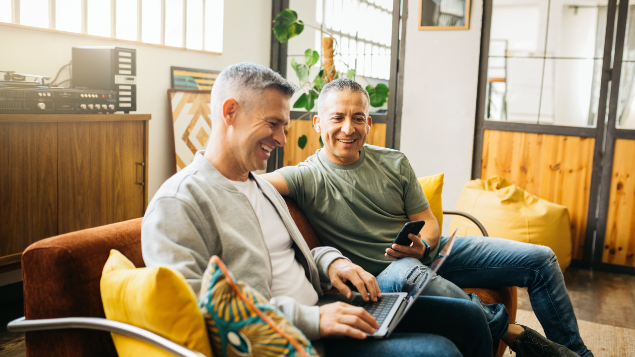 Gay couple on a couch using a laptop and going over their home finances in their living room.