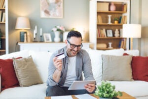 Smiling man holds tablet and credit card.