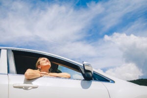 Woman sits relaxed in a car enjoying the sun and the scenic view