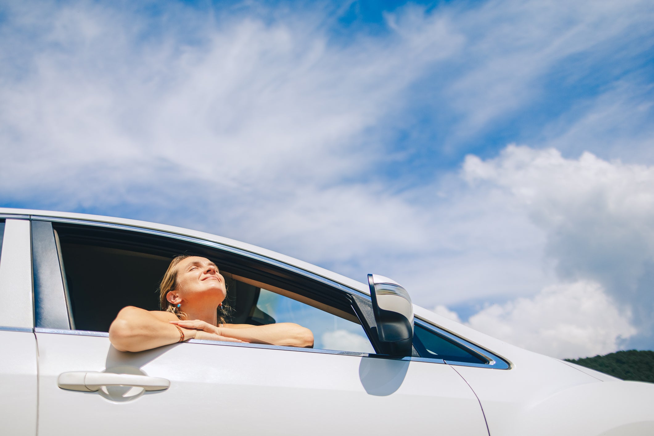 Woman sits relaxed in a car enjoying the sun and the scenic view