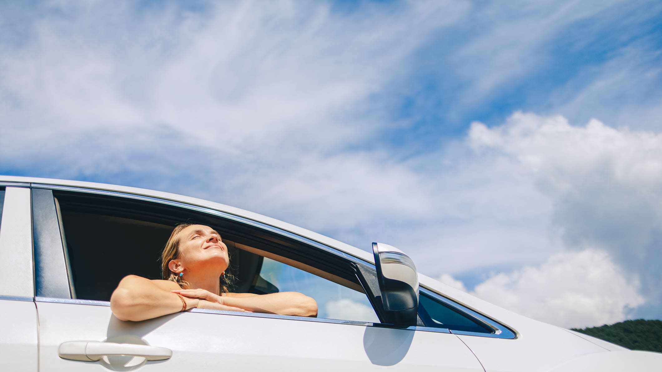 Woman sits relaxed in a car enjoying the sun and the scenic view