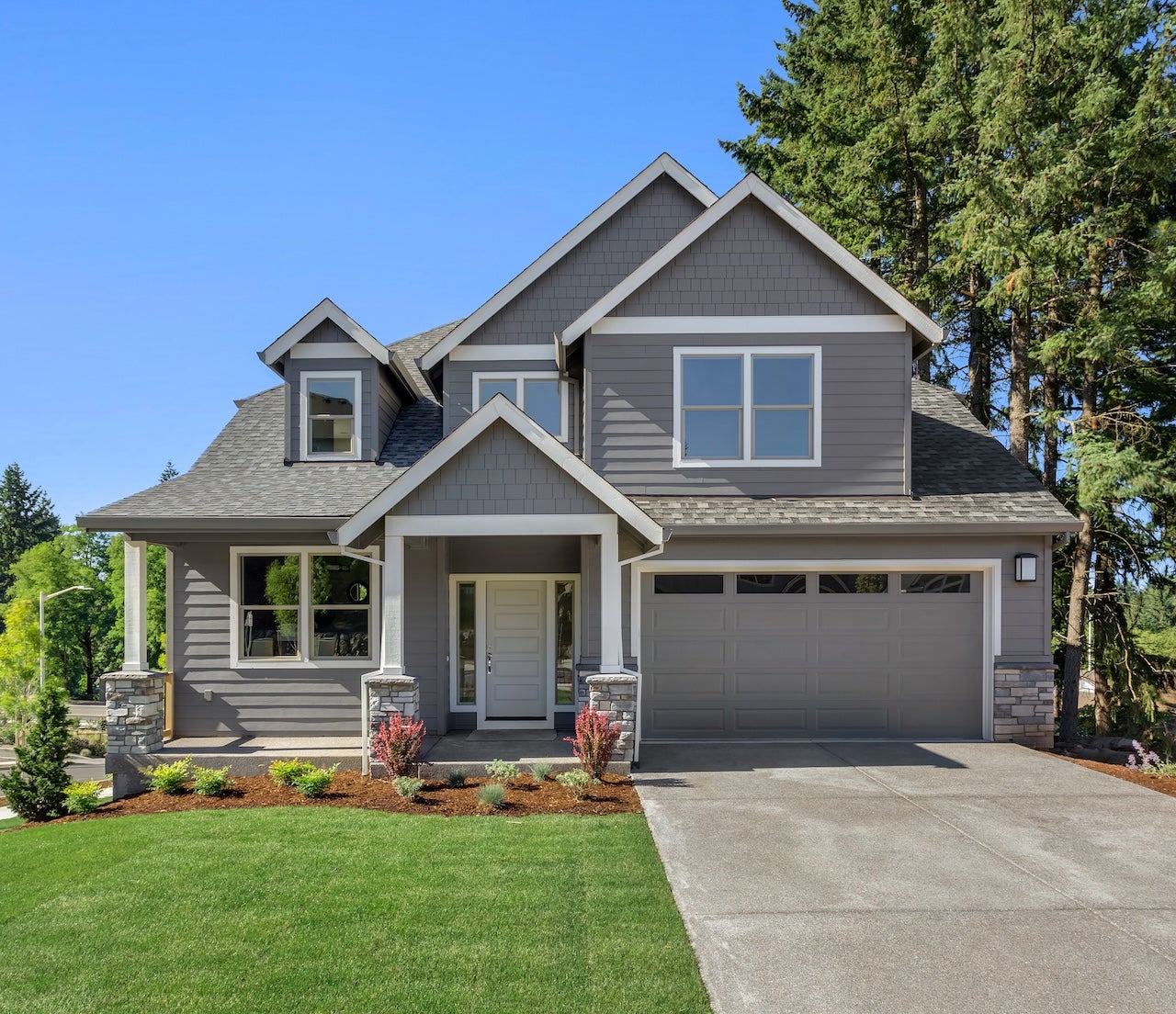 exterior of tidy gray suburban house with green lawn and blue sky