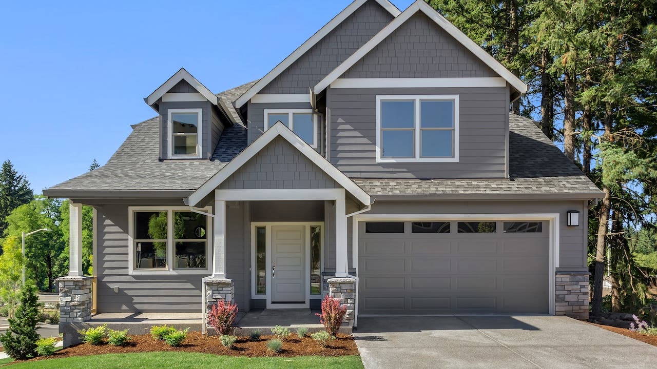 exterior of tidy gray suburban house with green lawn and blue sky