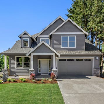 exterior of tidy gray suburban house with green lawn and blue sky