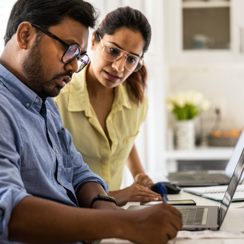 A couple works on their finances on a laptop in their kitchen.