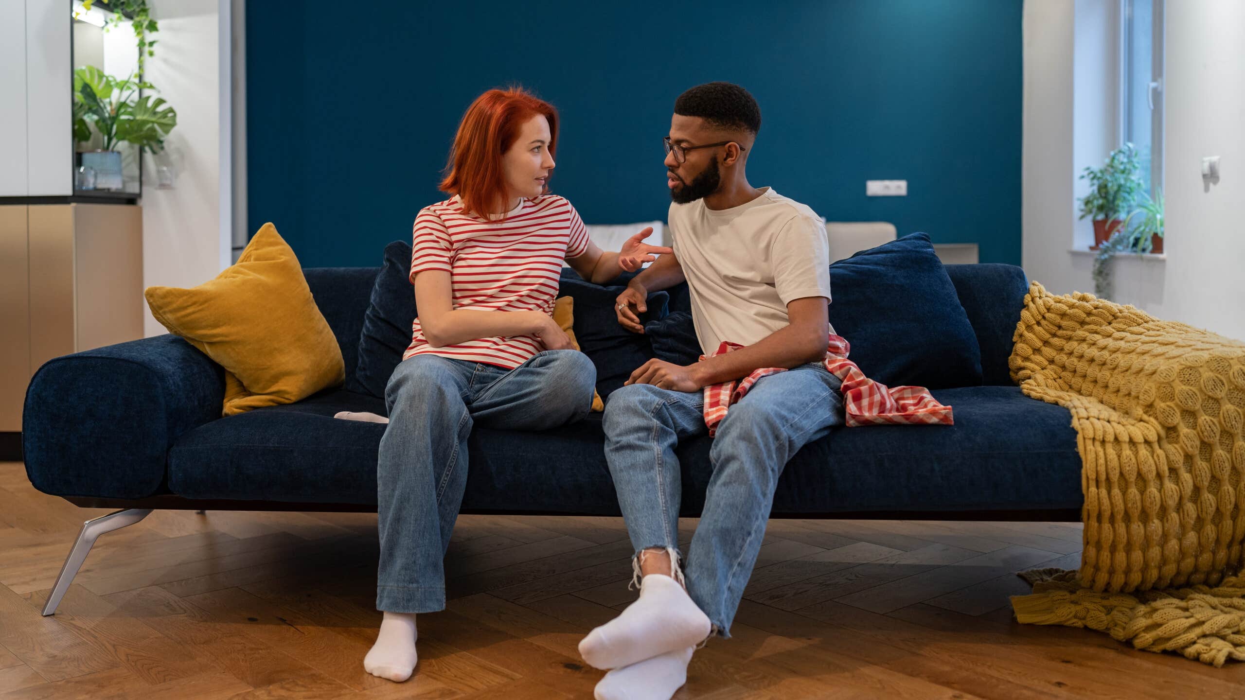 Man and woman sit on a couch with serious expressions.
