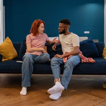 Man and woman sit on a couch with serious expressions.