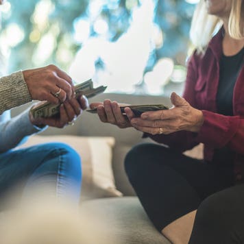 Two women exchanging money on a couch.