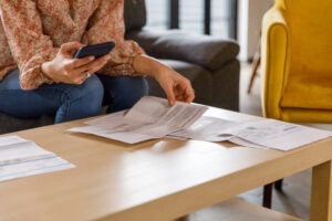 Woman holding her phone and looking at paperwork on the table