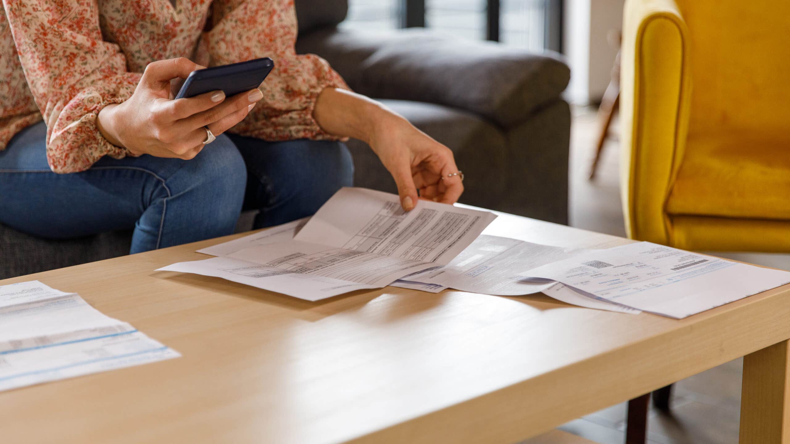 Woman holding her phone and looking at paperwork on the table