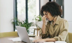 Young woman sits a computer with her head in her hand.