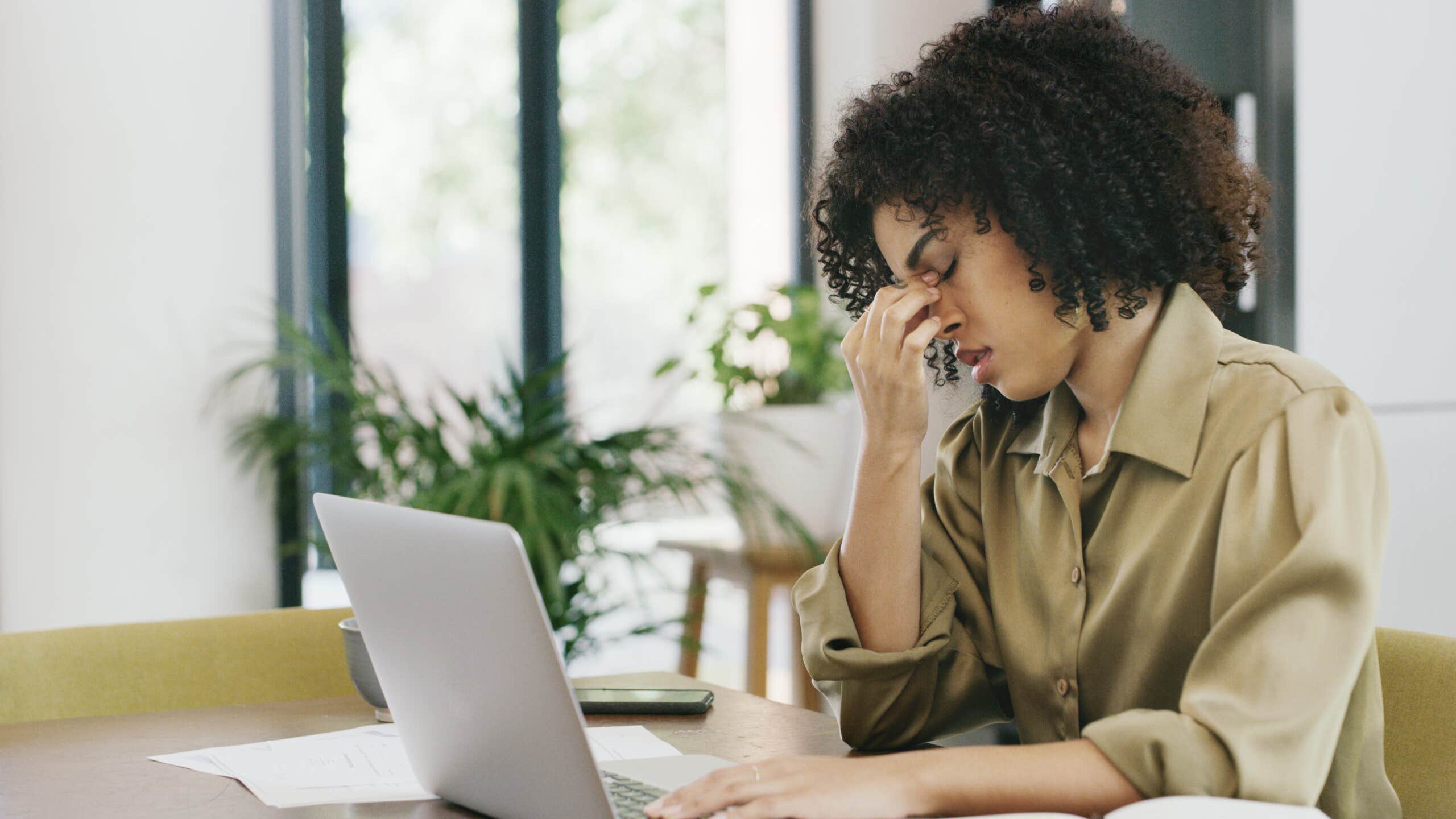 Young woman sits a computer with her head in her hand.