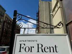A For Rent sign hangs in front of a city apartment building