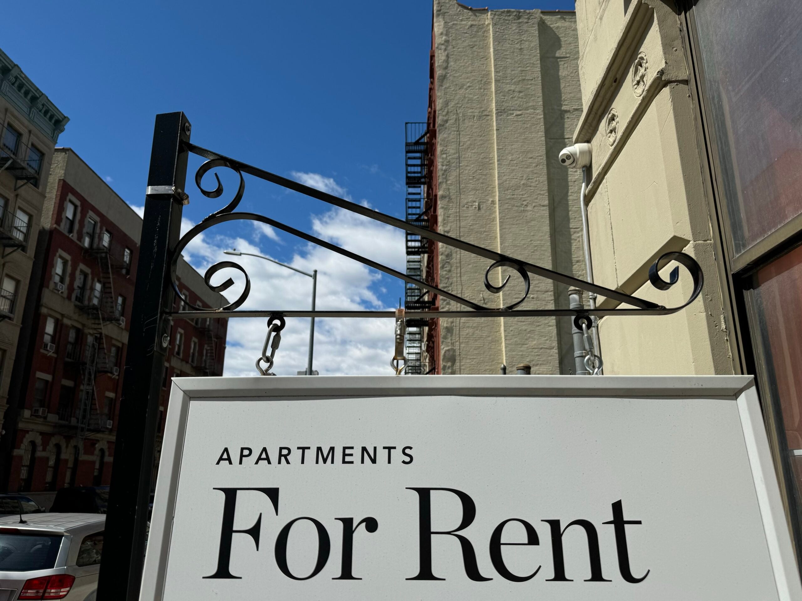 A For Rent sign hangs in front of a city apartment building
