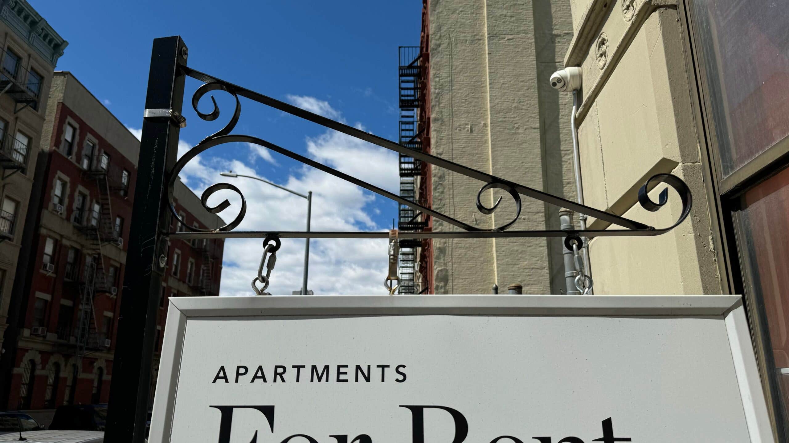 A For Rent sign hangs in front of a city apartment building