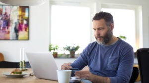 A middle aged white man uses a computer while looking at a credit card.