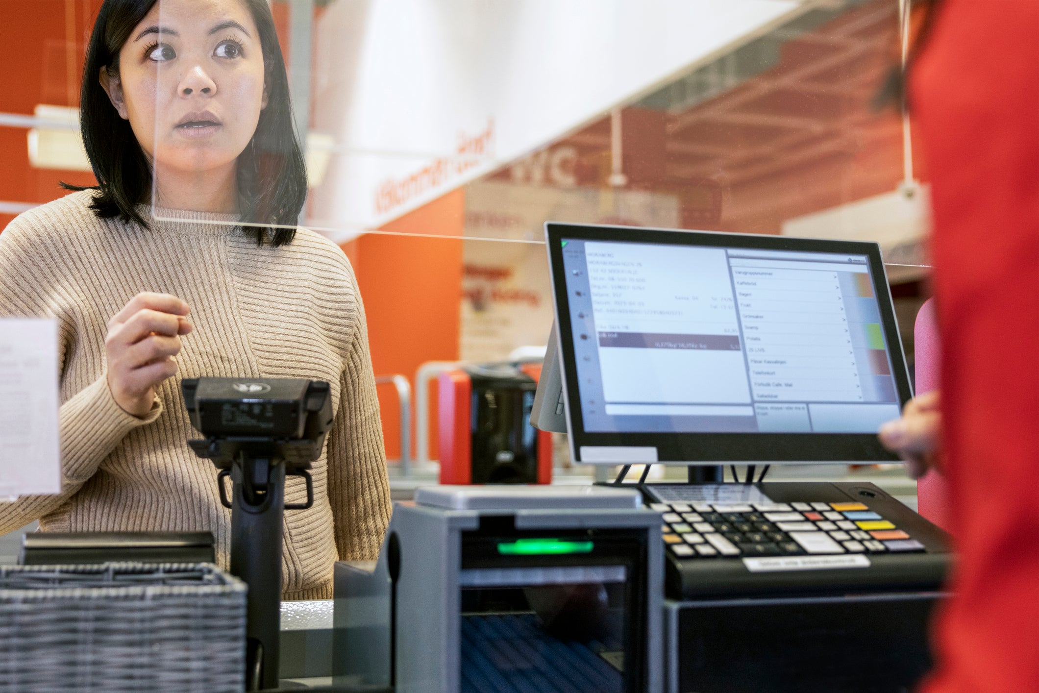 Young female customer talking to cashier at checkout in supermarket