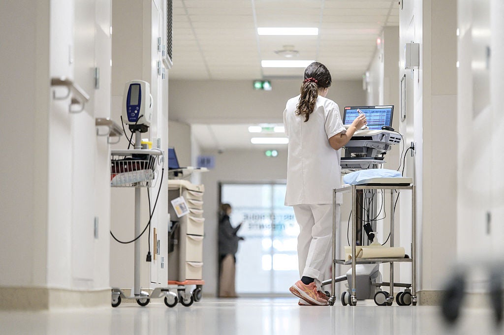 A nurse in a white coat walks along a white corridor with instruments and a monitoring or treatment cart in the neonatal or pediatric unit of the hospital in Pau, France, on December 1, 2025