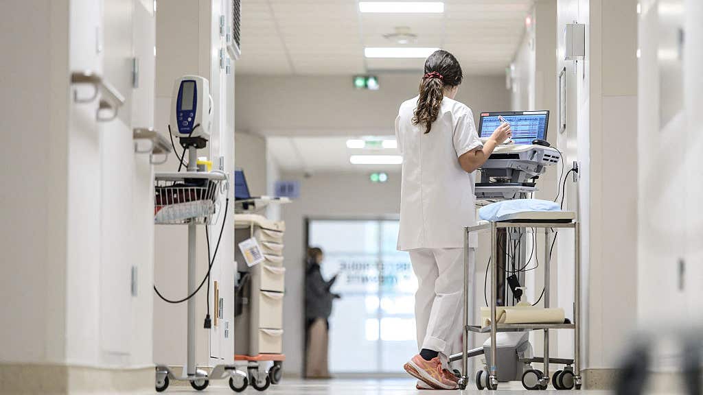 A nurse in a white coat walks along a white corridor with instruments and a monitoring or treatment cart in the neonatal or pediatric unit of the hospital in Pau, France, on December 1, 2025