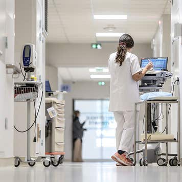 A nurse in a white coat walks along a white corridor with instruments and a monitoring or treatment cart in the neonatal or pediatric unit of the hospital in Pau, France, on December 1, 2025