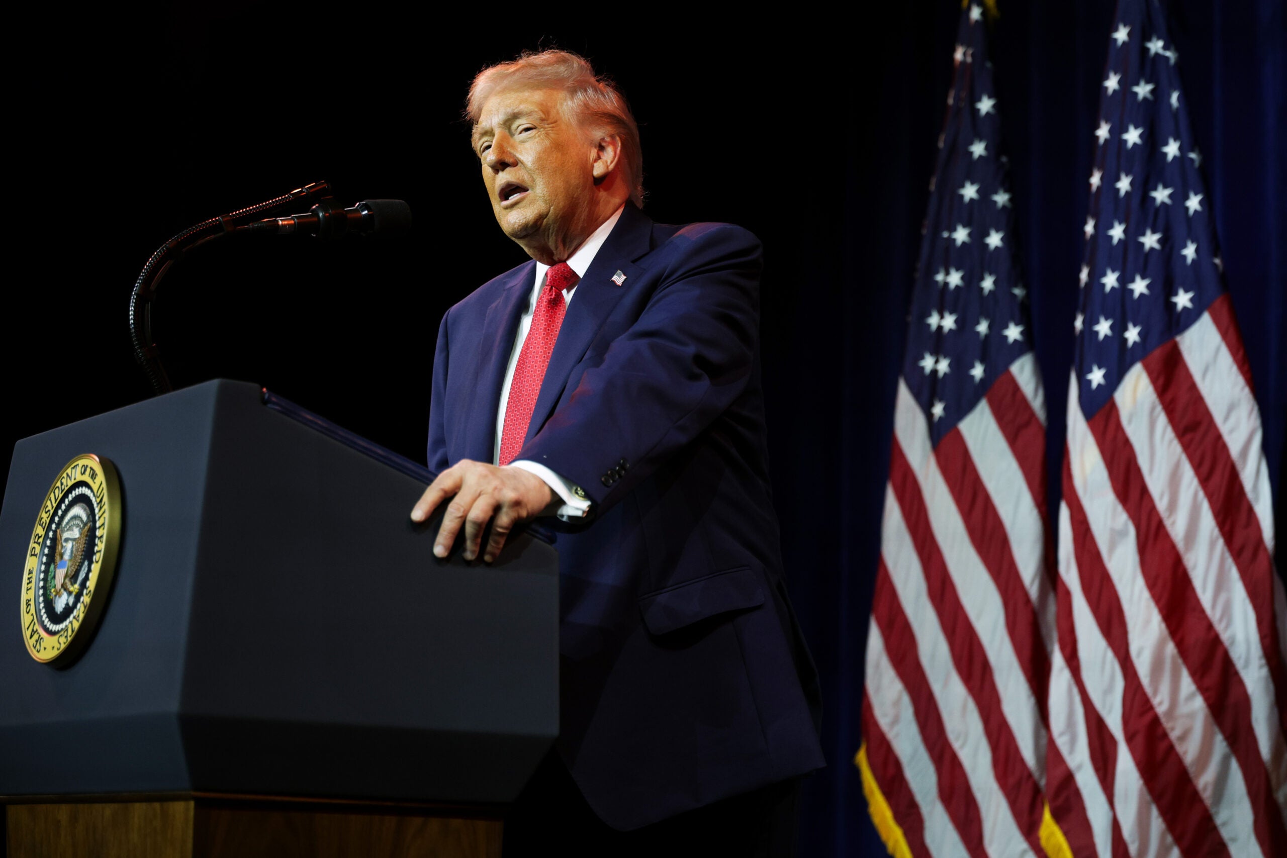 President Donald Trump speaks behind a podim with a U.S. flag in the background