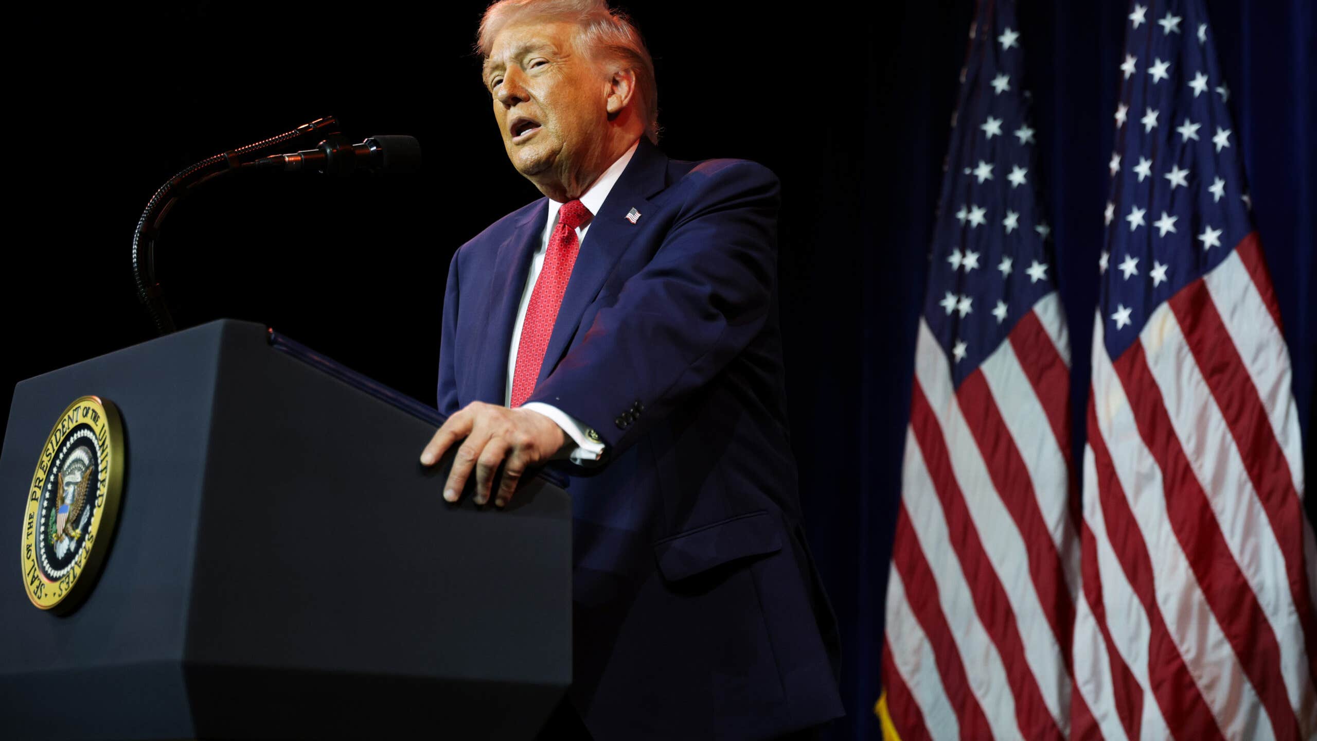President Donald Trump speaks behind a podim with a U.S. flag in the background