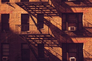 Shadows fall across a brick apartement building and its fire escapes