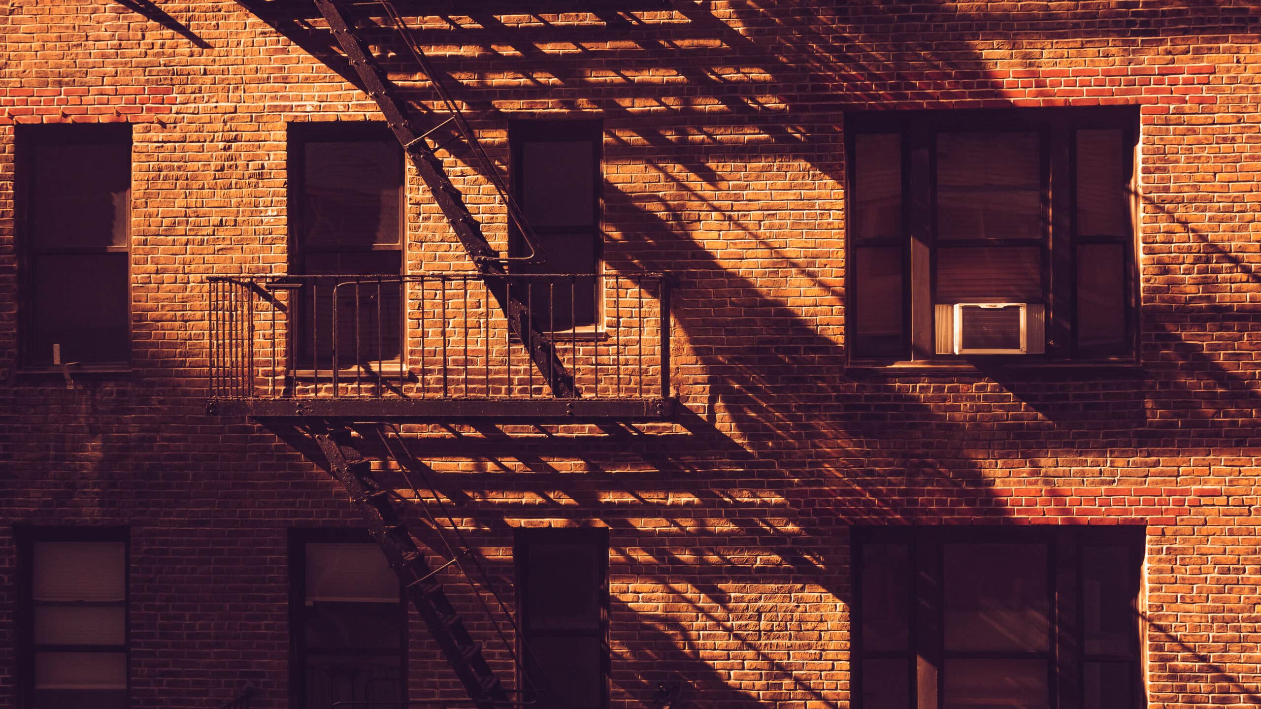 Shadows fall across a brick apartement building and its fire escapes