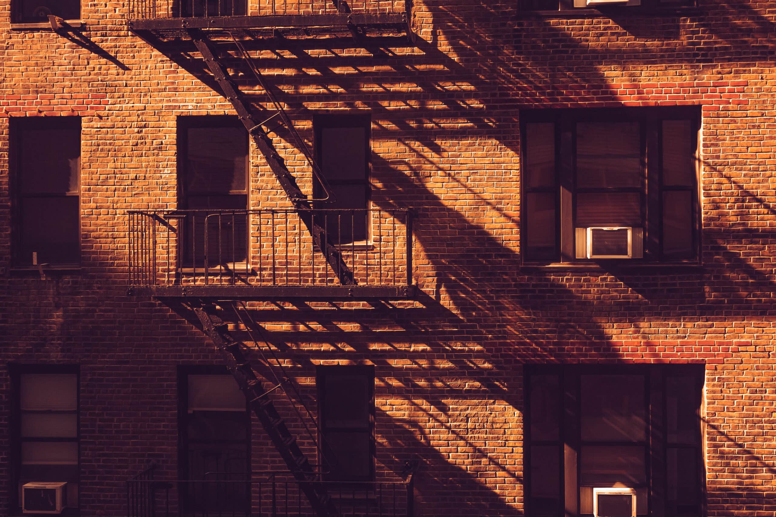 Shadows fall across a brick apartement building and its fire escapes