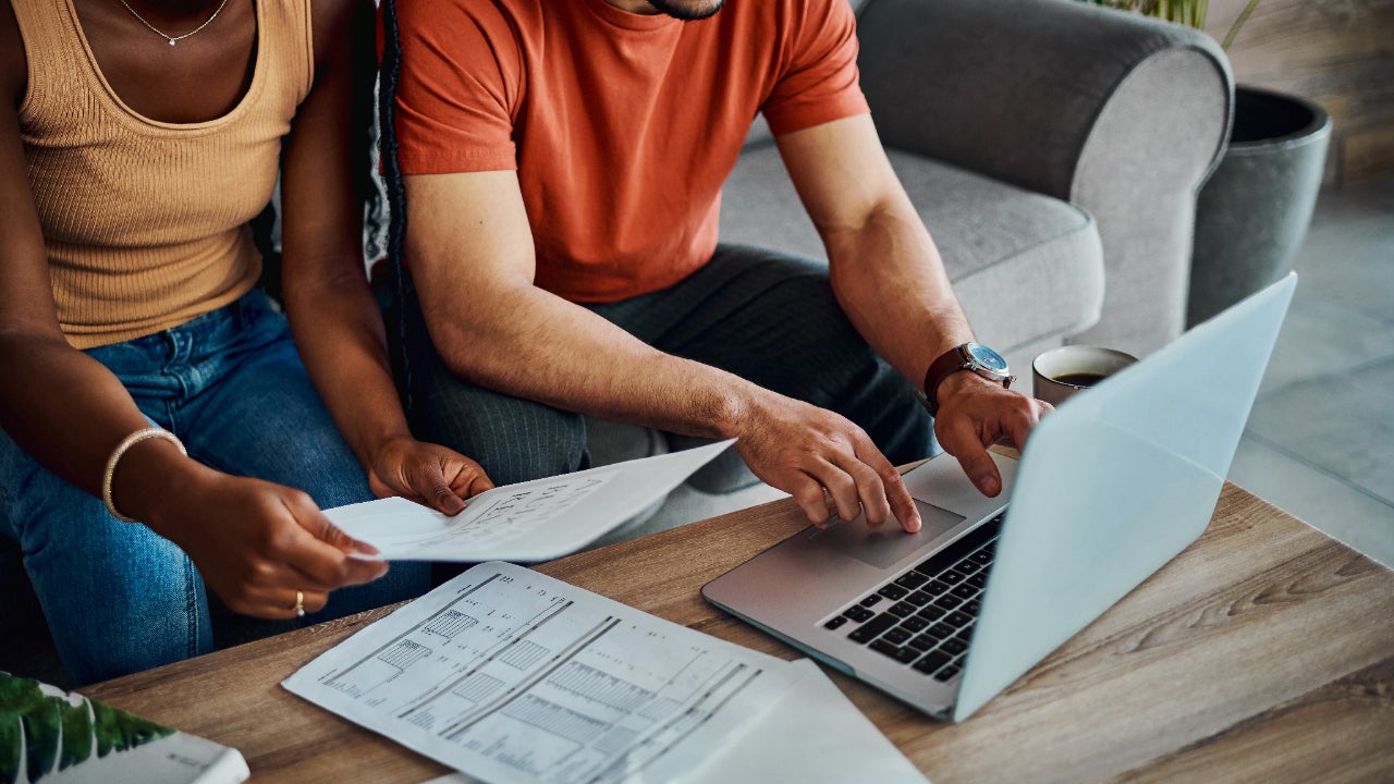 A man and a woman work together on a laptop while reading paperwork.