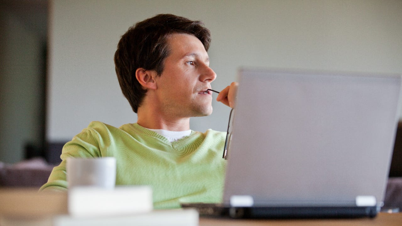 Man sitting in front of his laptop looking pensive while holding his glasses.