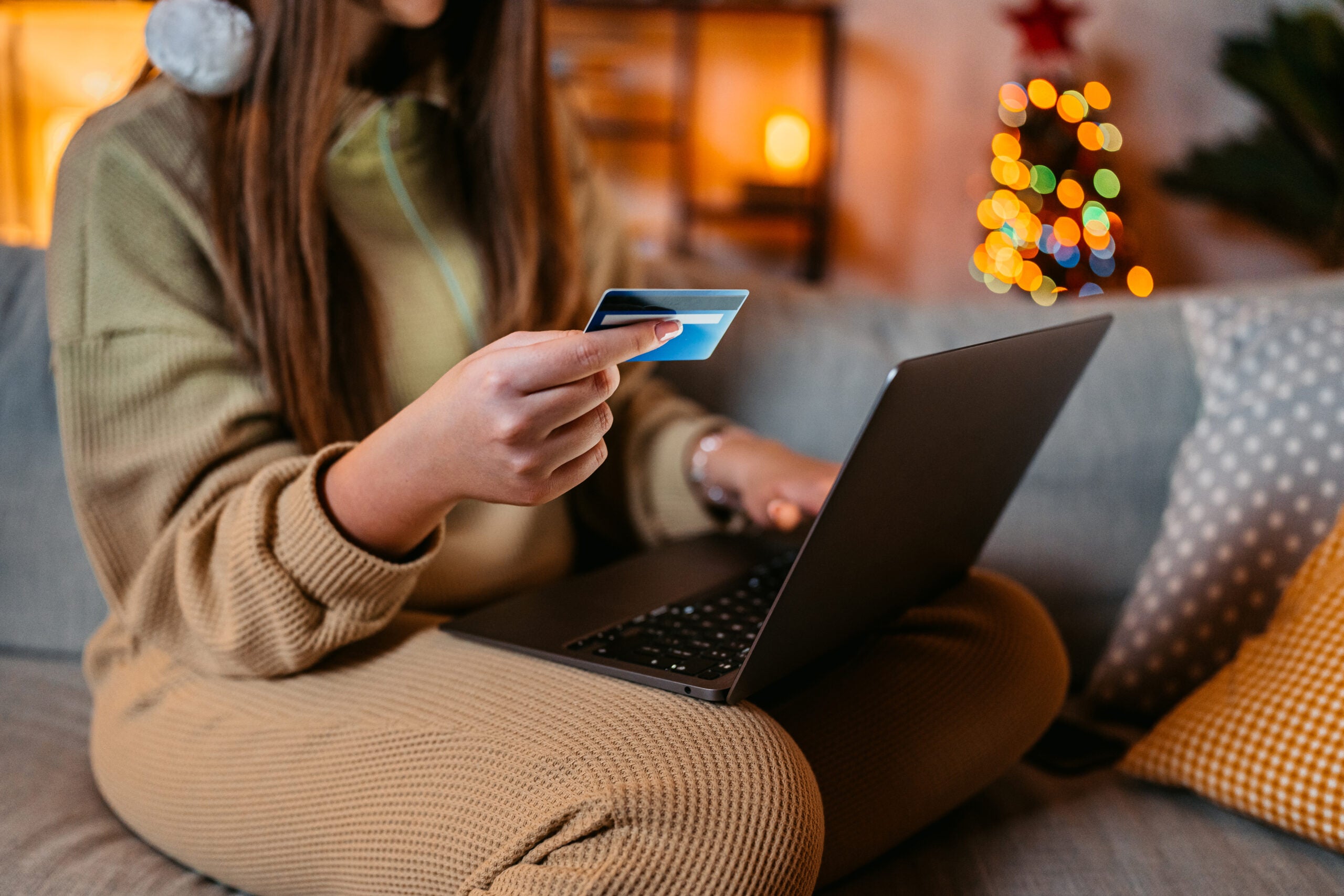 A woman holds a credit card and online shops with holiday lights in the background