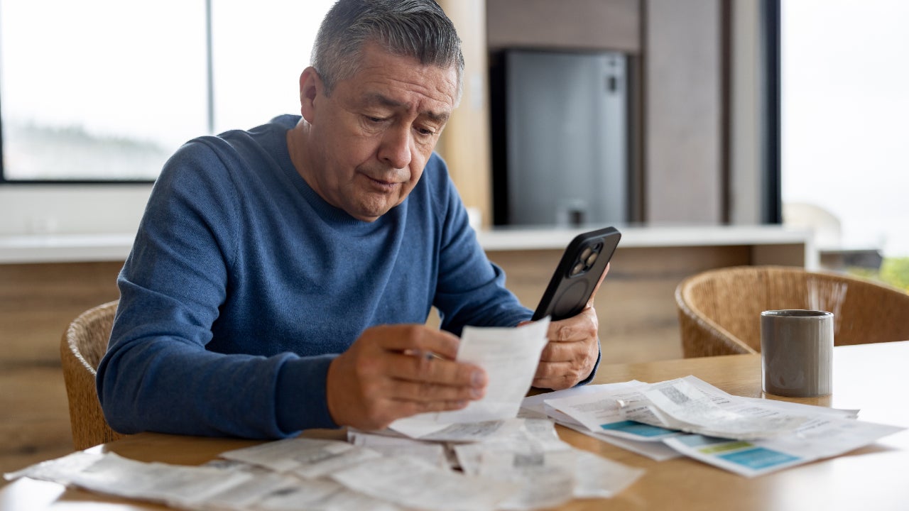A man reviews receipts and paperwork while also holding his phone.