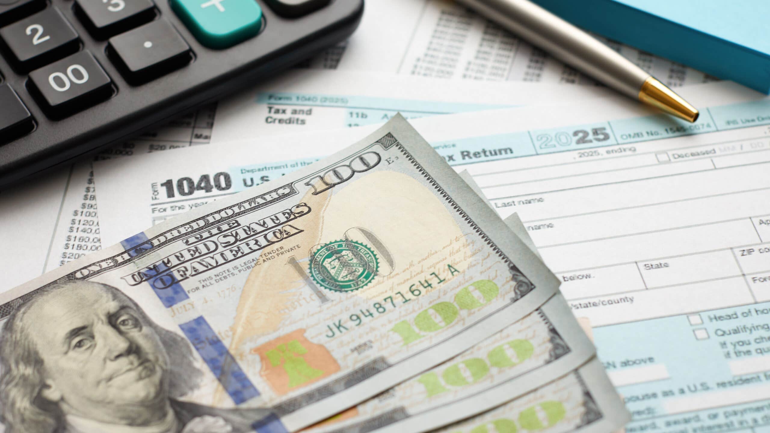 $100 bills lay on top of a 1040 U.S. Federal tax form.