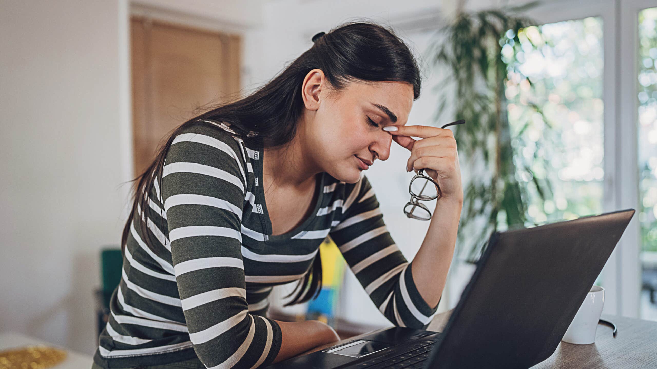 Woman looks stressed with her head in her hand at a laptop.
