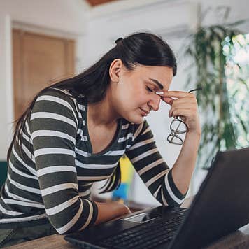 Woman looks stressed with her head in her hand at a laptop.