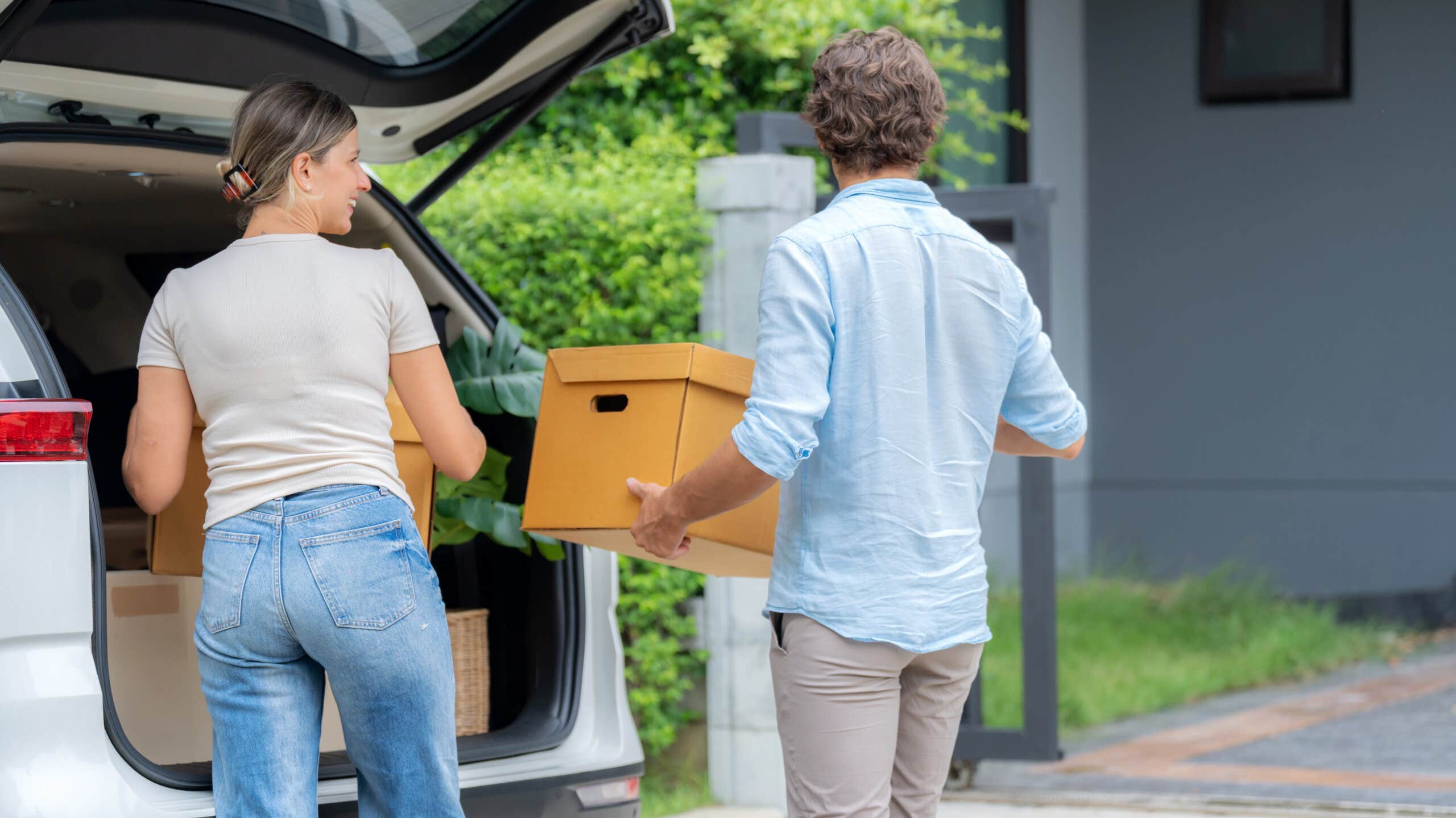Young couple unloads boxes from the back of a vehicle.