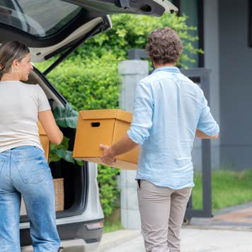 Young couple unloads boxes from the back of a vehicle.