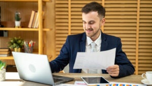 A man reviews paperwork while using a laptop.
