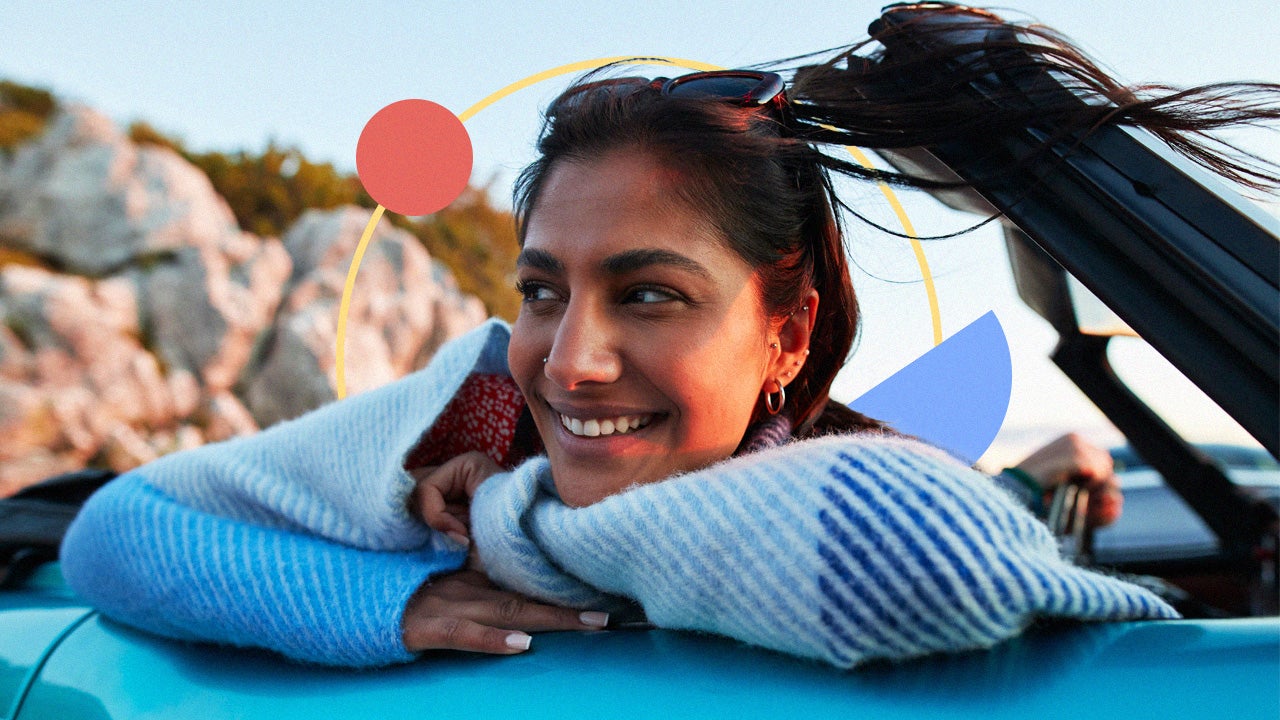 A person leaning on the car door of a convertible and enjoying the wind in their hair.